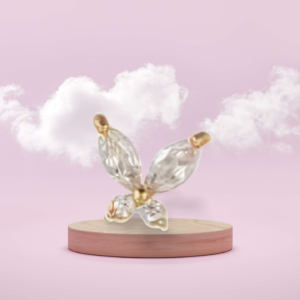 Butterfly-inspired earrings with translucent crystal wings and gold accents, displayed on a wooden pedestal against a pastel pink background with clouds.